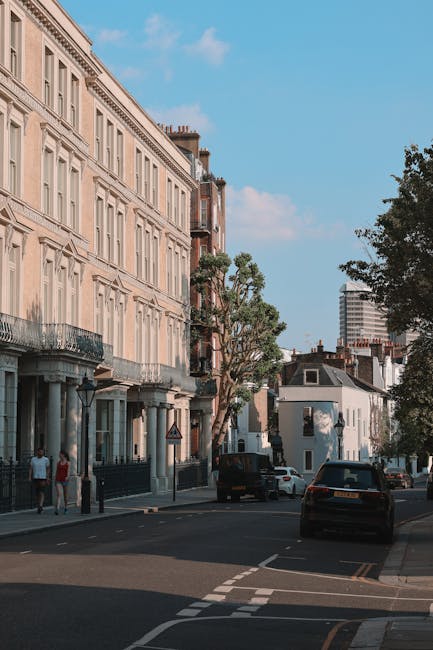 A row of Victorian-style terraced houses situated on a city street under a clear blue sky. The residences feature ornate white decorative ironwork railings and trim, with large bay windows on the uppe